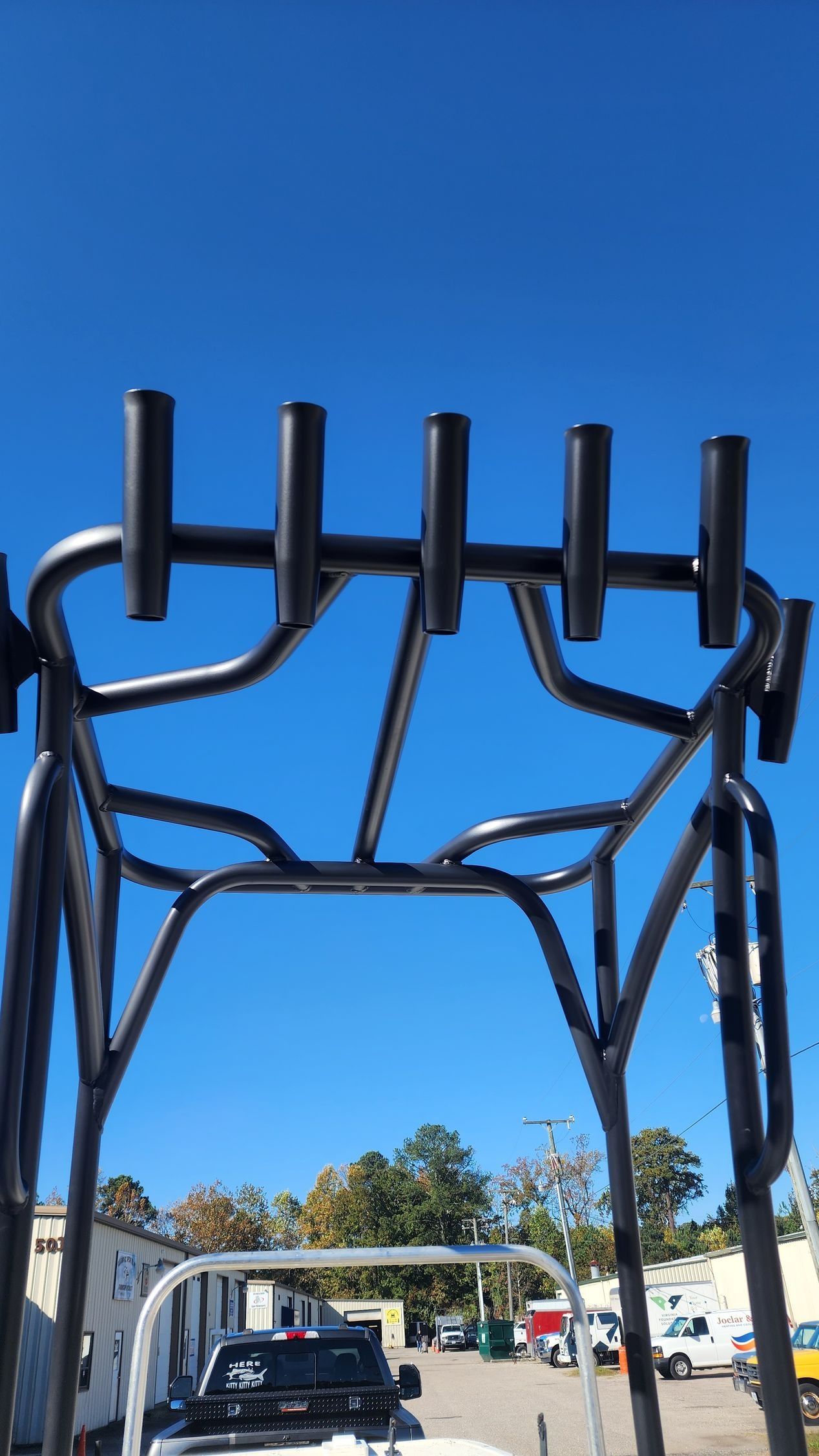 Black metal boat T-top with six fishing rod holders against a clear blue sky.
