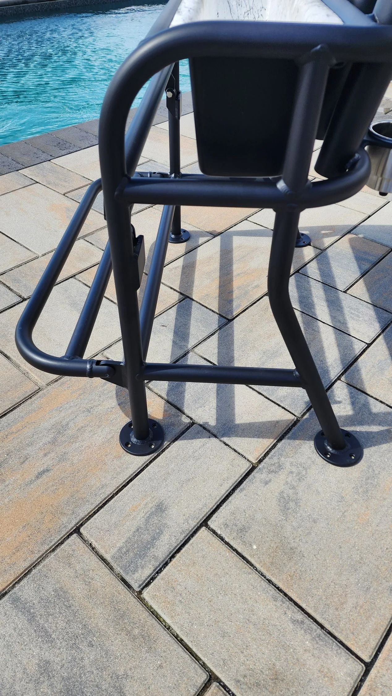 Black metal bar stool on a brick patio next to a pool.