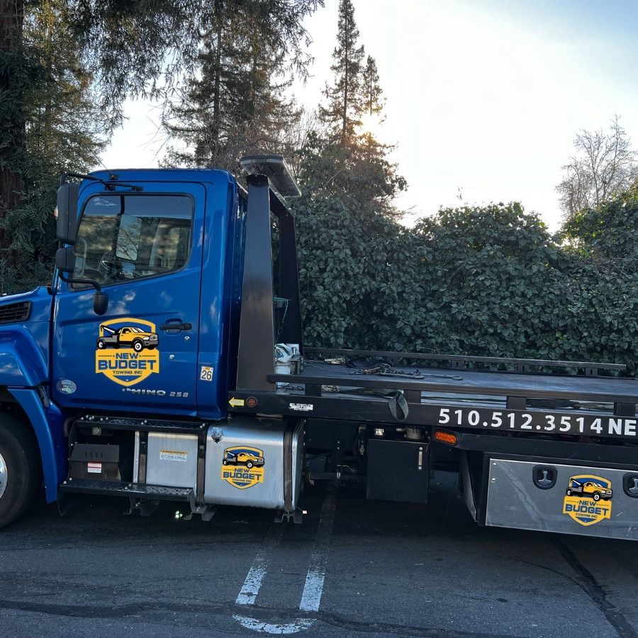 Blue Budget towing truck with flatbed, parked outdoors. Phone number 510.512.3514 displayed.
