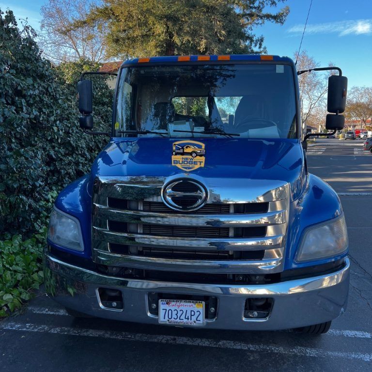 Blue delivery truck with logo and California license plate parked next to green bushes.
