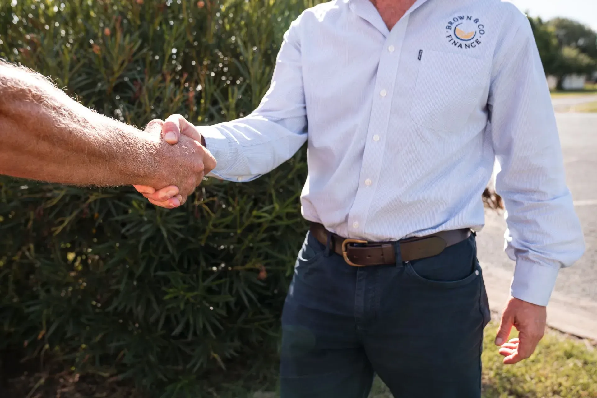 Two Men Are Shaking Hands In Front Of A Bush — Brown & Co Finance in Toowoomba, QLD