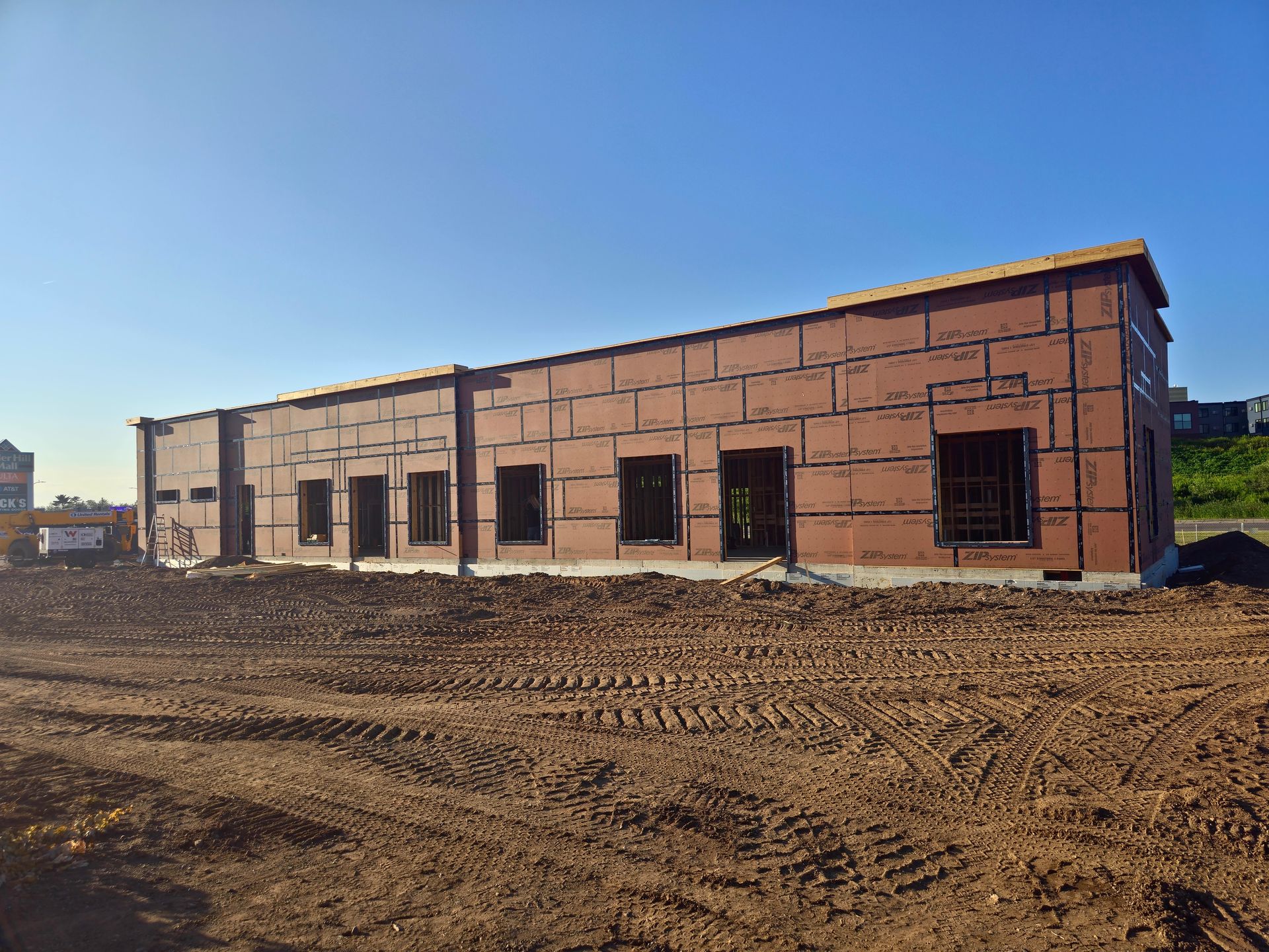 Building under construction with brown exterior, several window openings, and a dirt foreground.