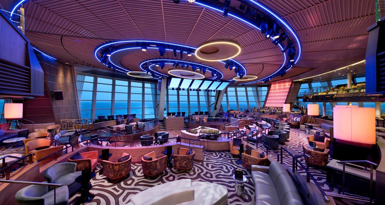 Interior of a circular bar on a cruise ship with panoramic ocean views and blue and purple lighting.