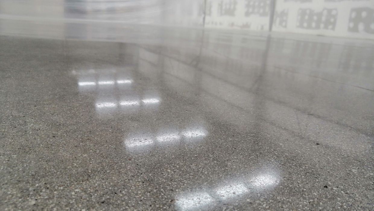 Primer plano de un suelo de hormigón pulido que muestra reflejos de luz y una superficie texturizada y moteada.