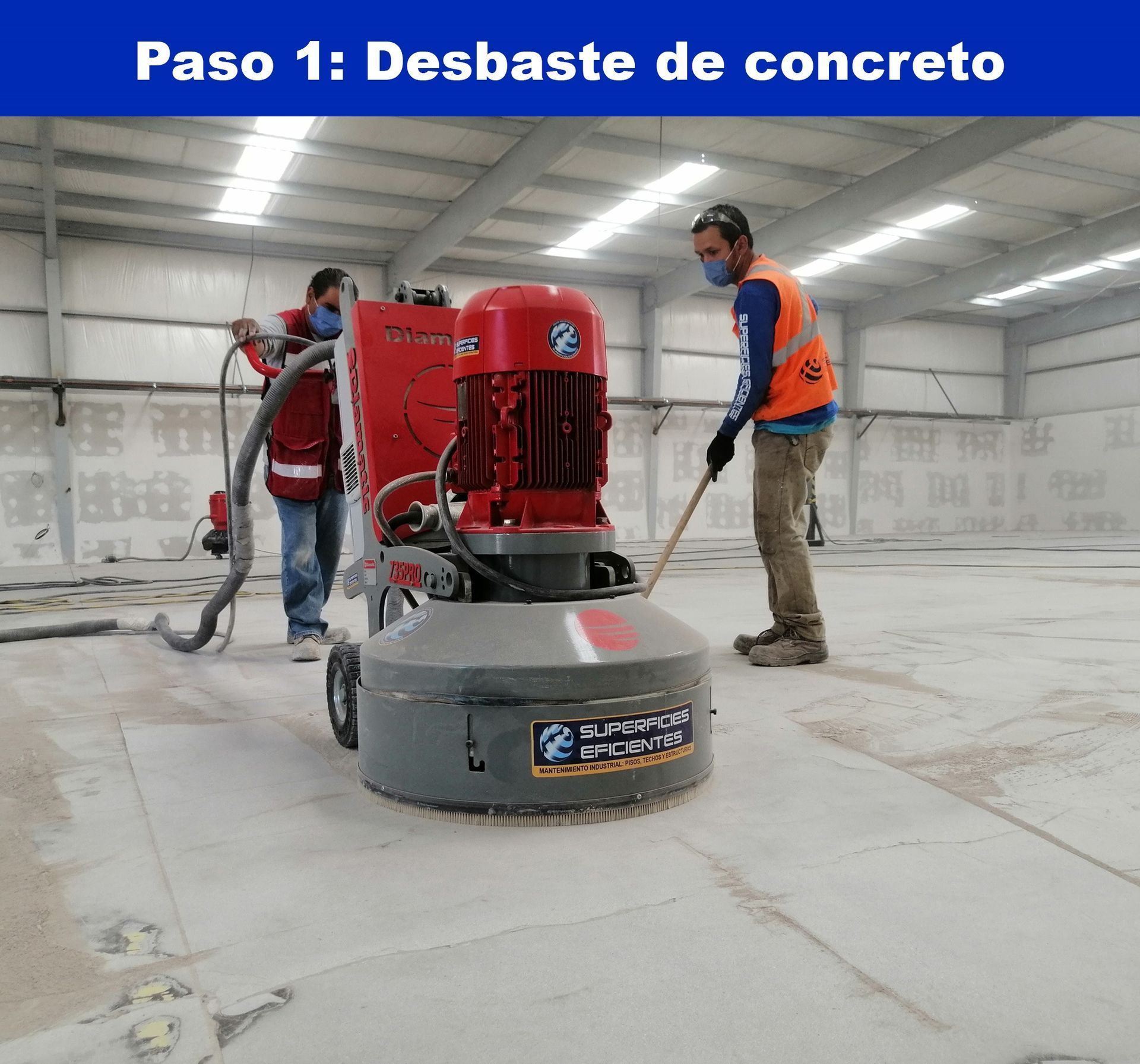 Dos trabajadores utilizan una pulidora industrial de gran tamaño sobre una superficie de hormigón en un almacén sin terminar.