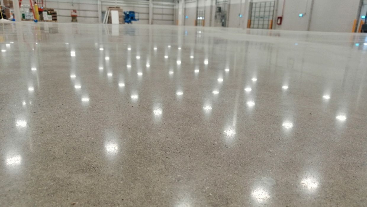 En un almacén, un gran suelo de hormigón gris pulido refleja las luces del techo, creando una superficie brillante y reluciente.