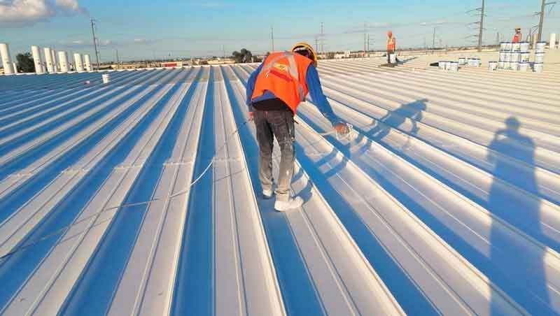 Una persona que lleva un chaleco naranja de alta visibilidad trabaja en un gran tejado de chapa ondulada de color blanco brillante.