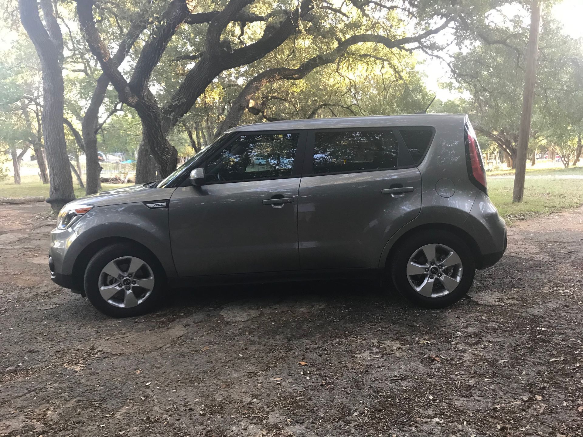 Side view of car parked on a gravel driveway with trees in the background.