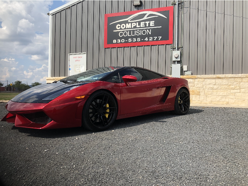 A red sports car is parked in front of a complete collision building.