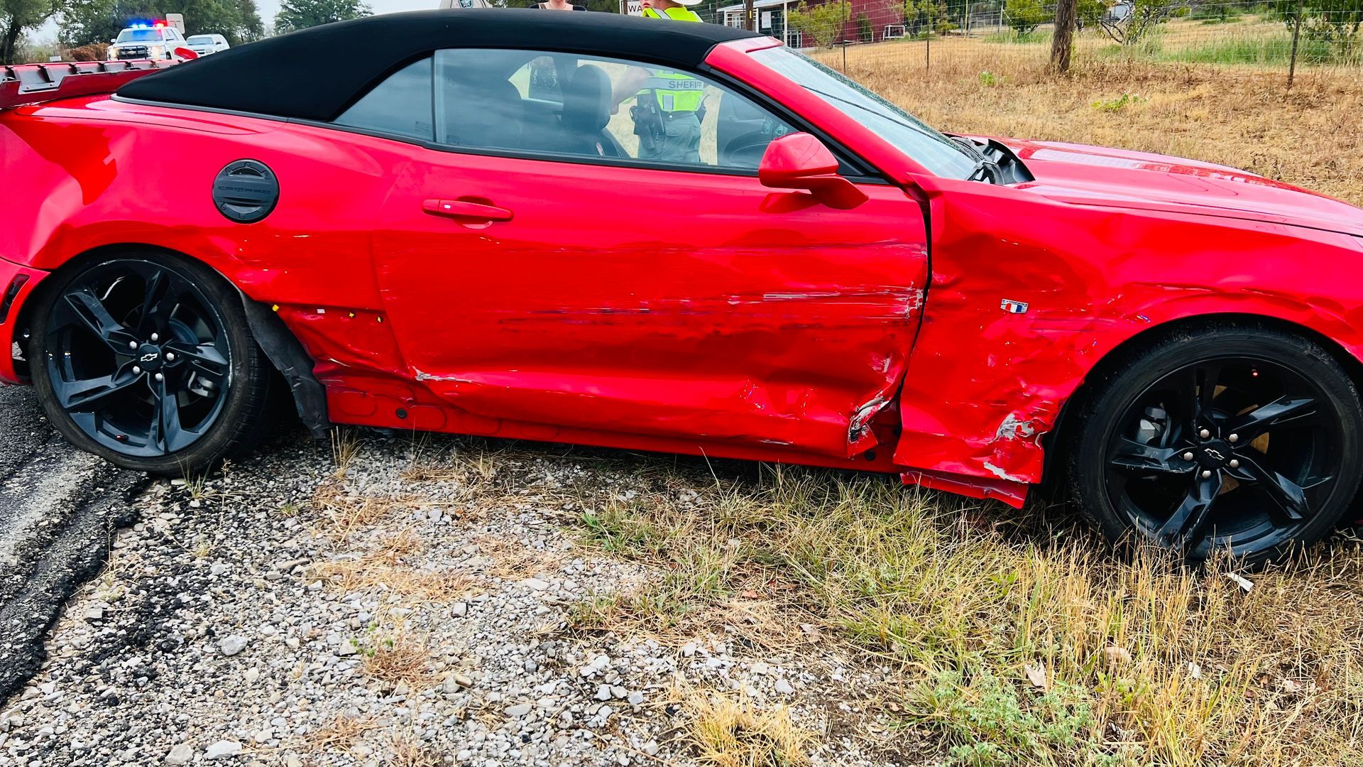 A red convertible car with a damaged side is parked on the side of the road.