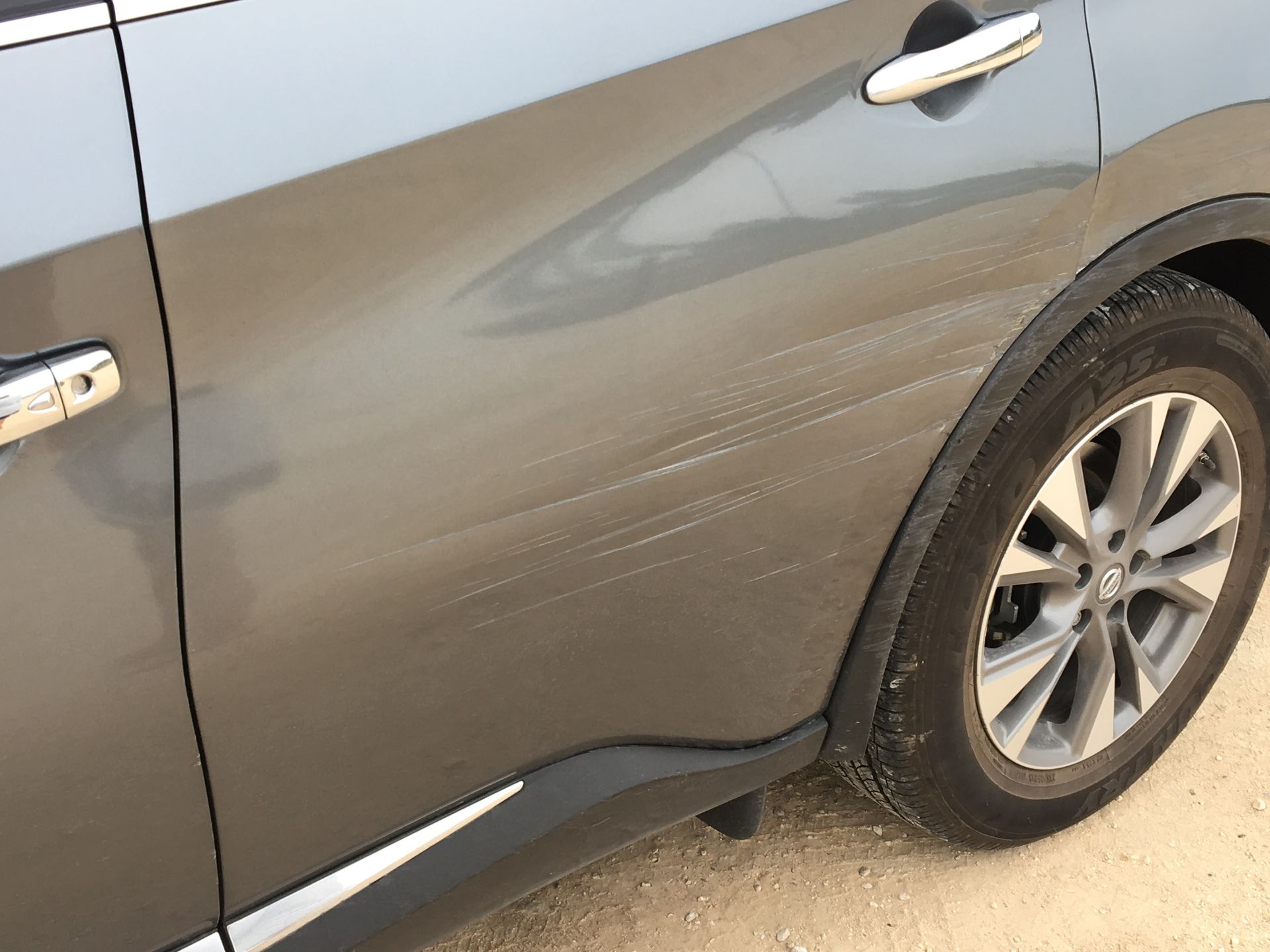 A gray car is parked on a dirt road.