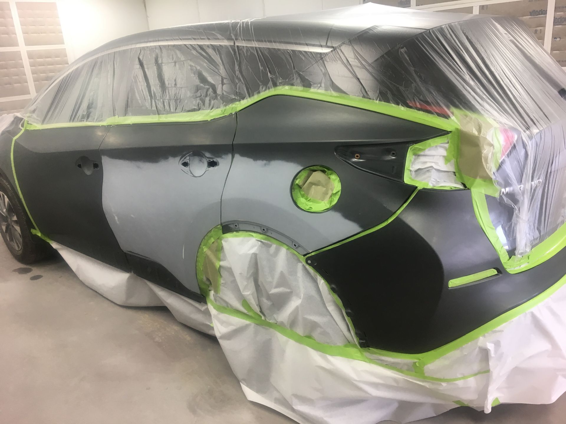 A car is covered in plastic and tape and is being painted.