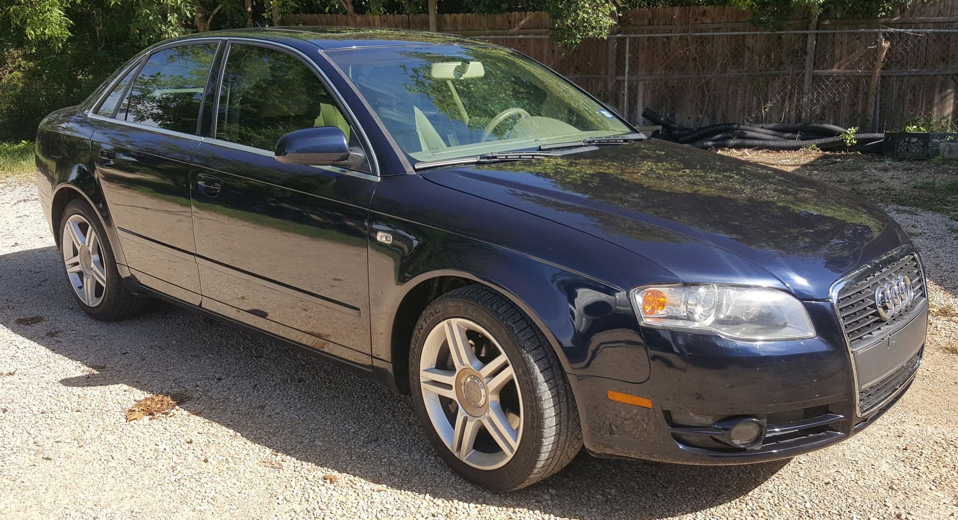 A blue audi a4 is parked in a gravel lot.