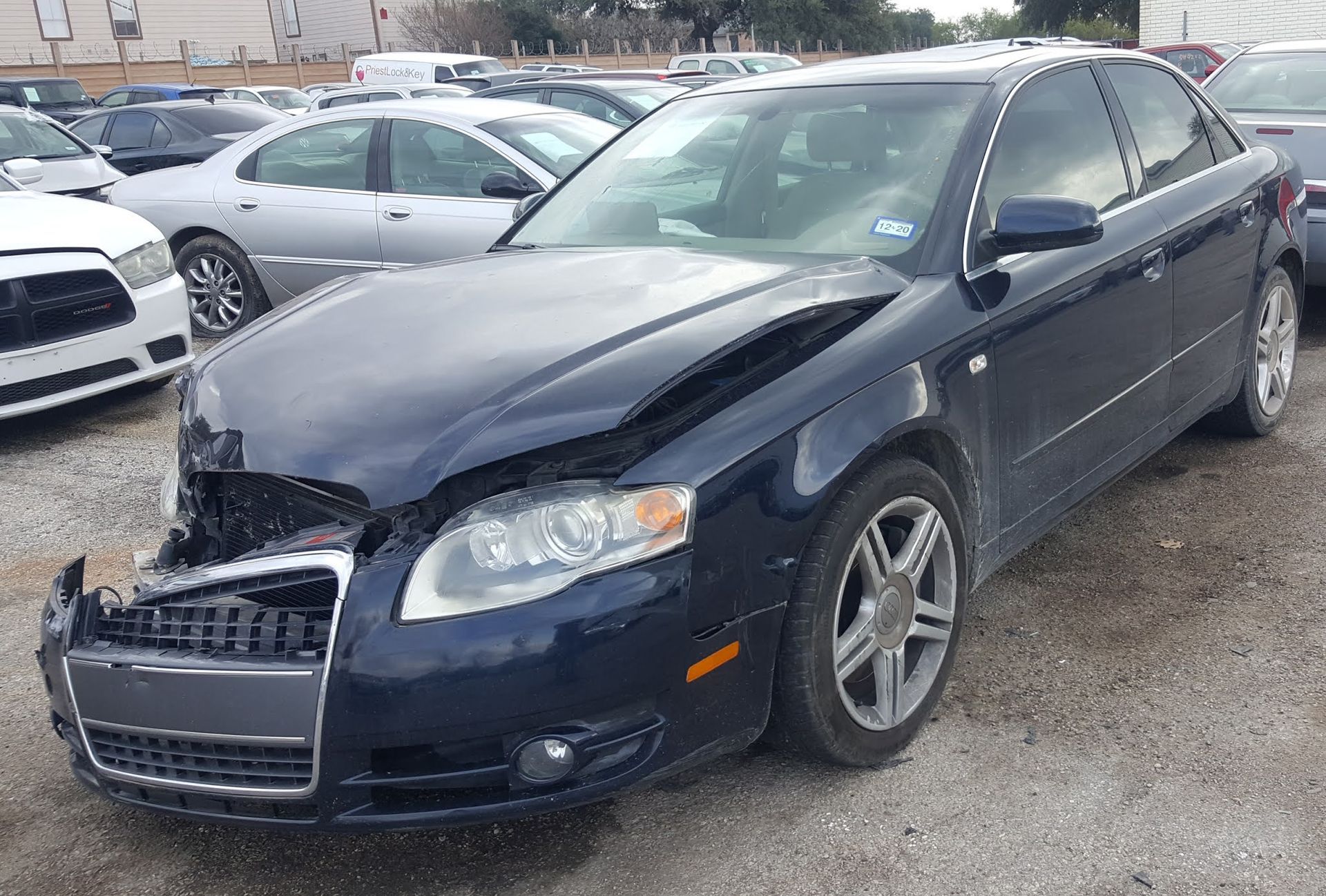 A blue car with a damaged hood is parked in a lot.
