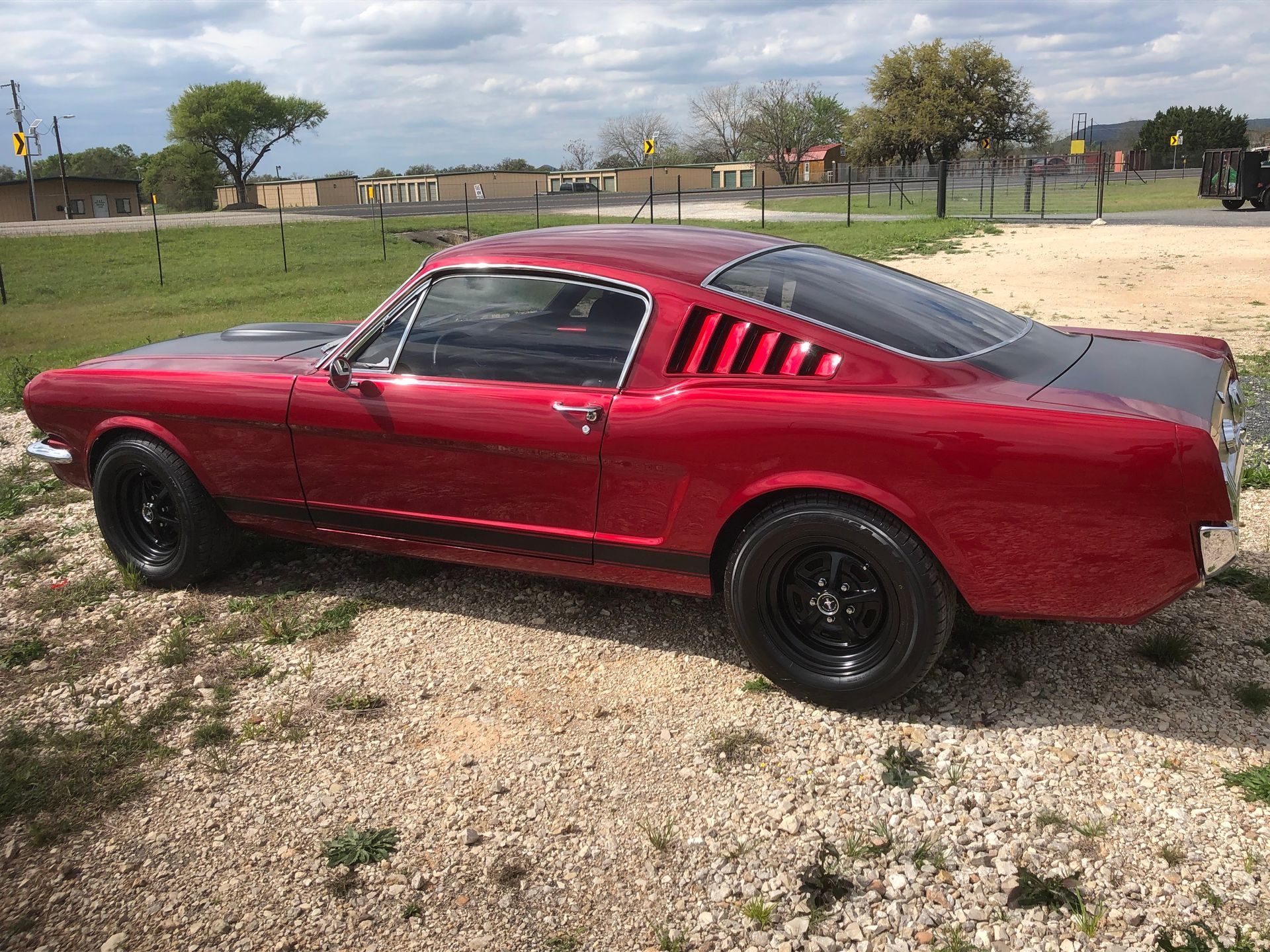 A red mustang is parked in a gravel lot.