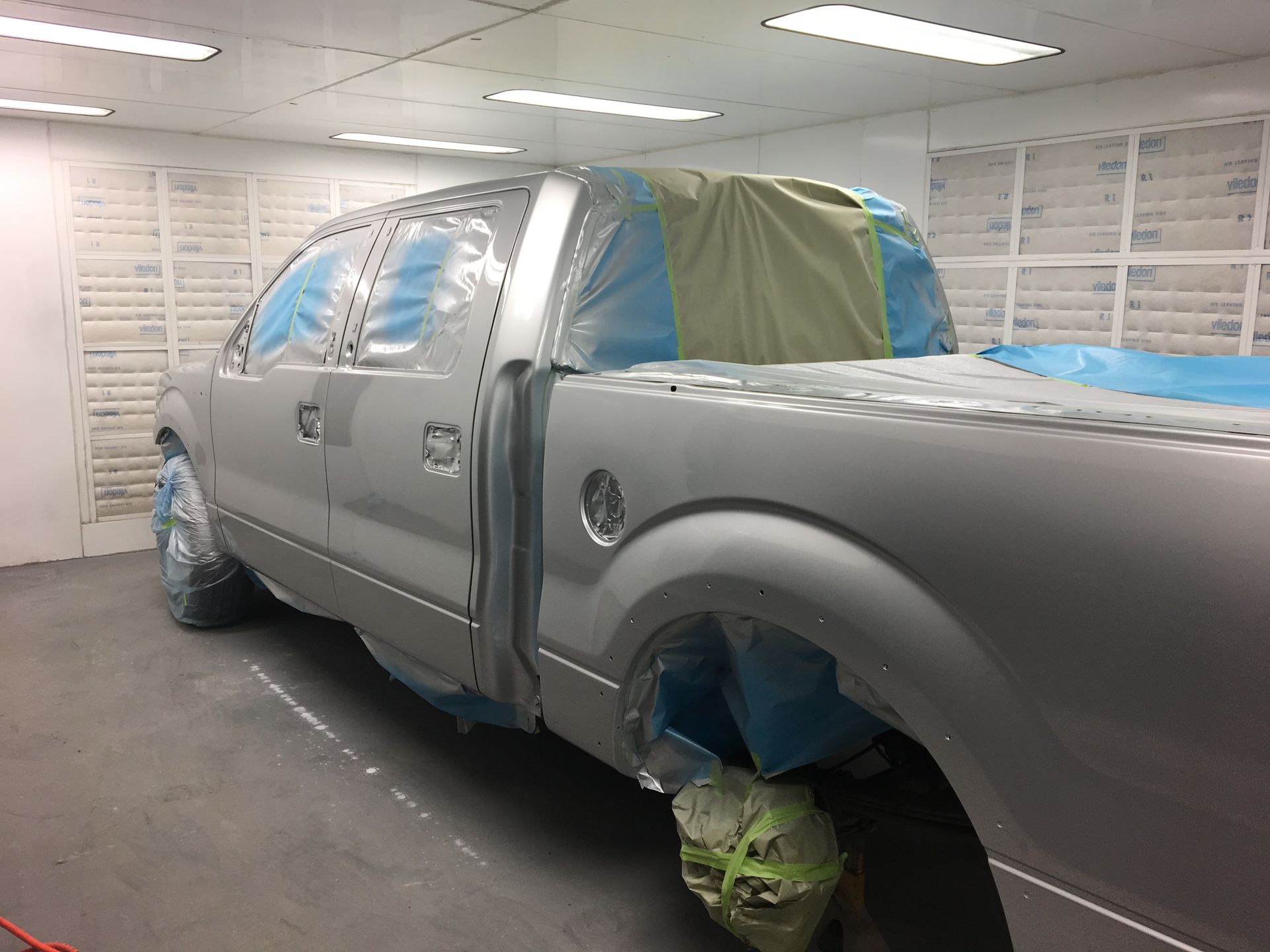 A silver truck is being painted in a paint booth.