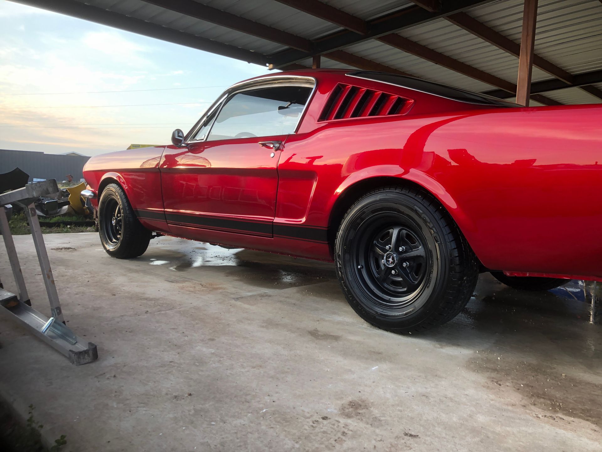 A red mustang is parked under a roof in a garage.