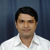 A man in a white shirt is standing in front of a blue curtain.