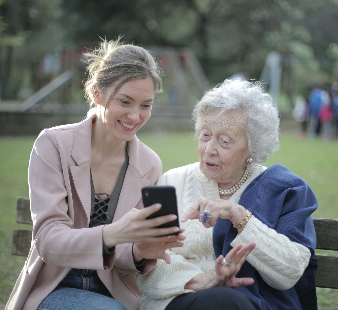 two women sat on a bench looking interestedly at a mobile phone
