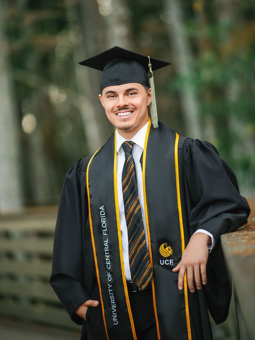 Bride and groom walking hand-in-hand under purple wisteria, brick wall on left, greenery on both sides.