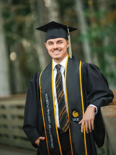 Bride and groom walking hand-in-hand under purple wisteria, brick wall on left, greenery on both sides.