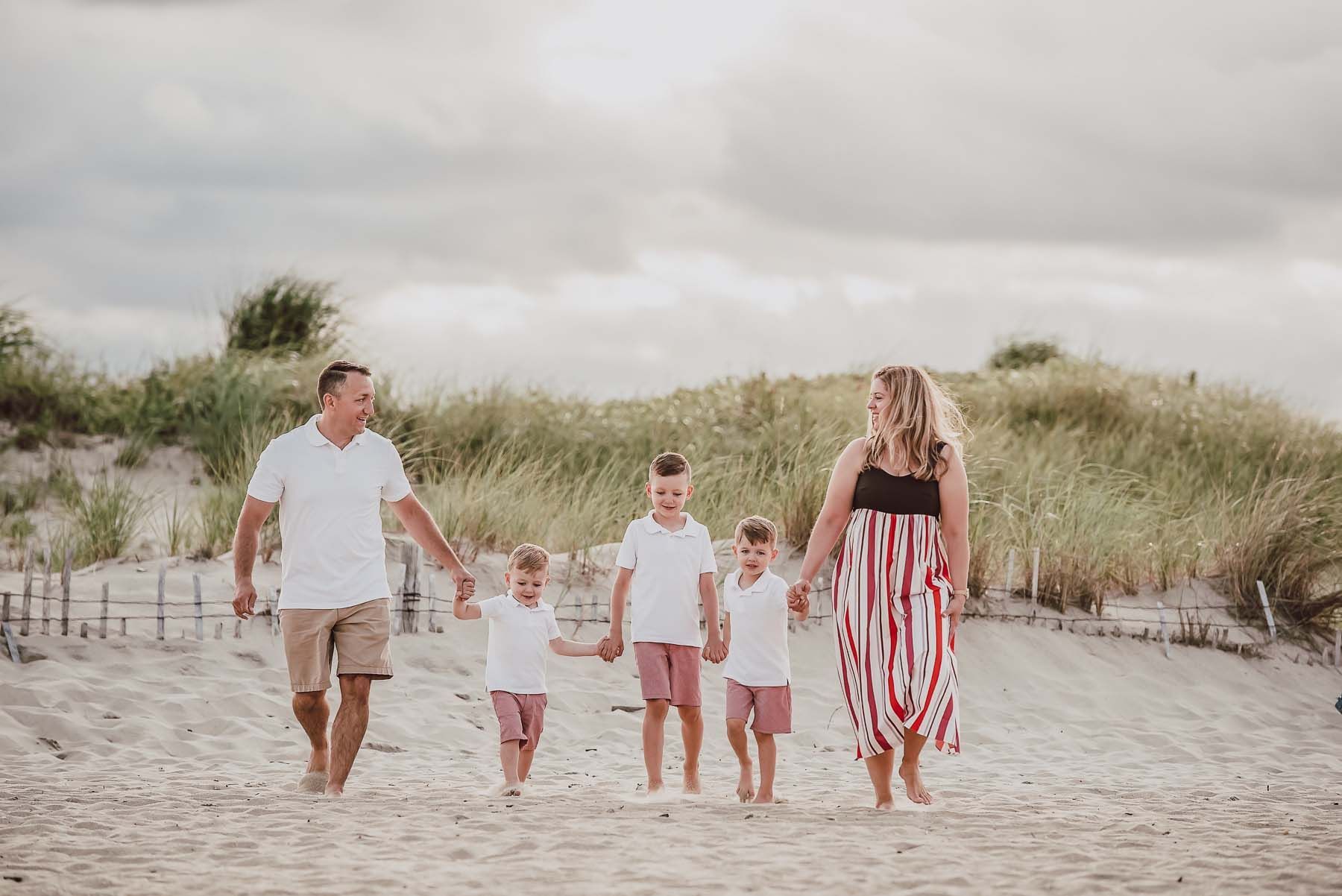 Family of five walking on a sandy beach, holding hands. The parents and three children are smiling.