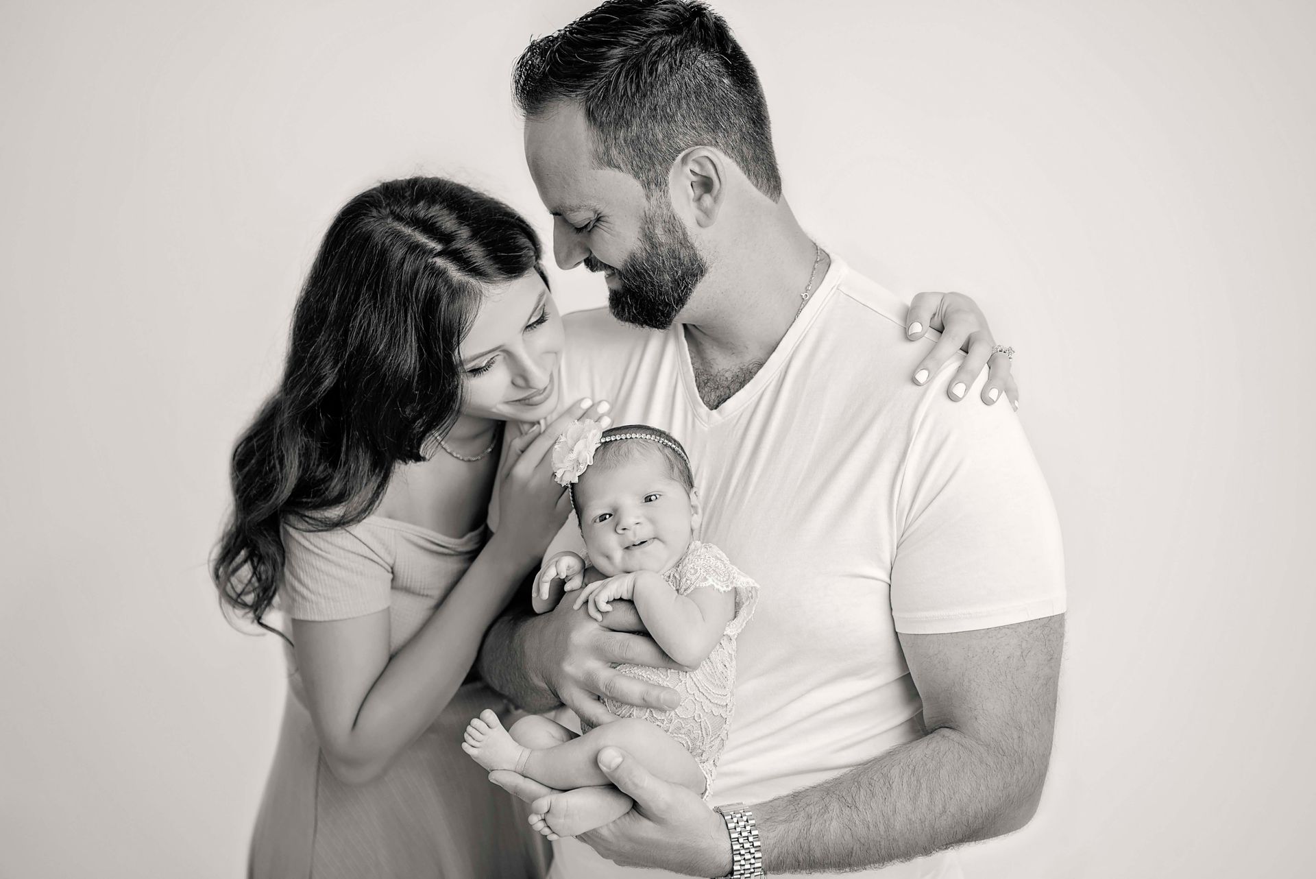 Family of three in black and white: parents gaze at newborn baby they hold.
