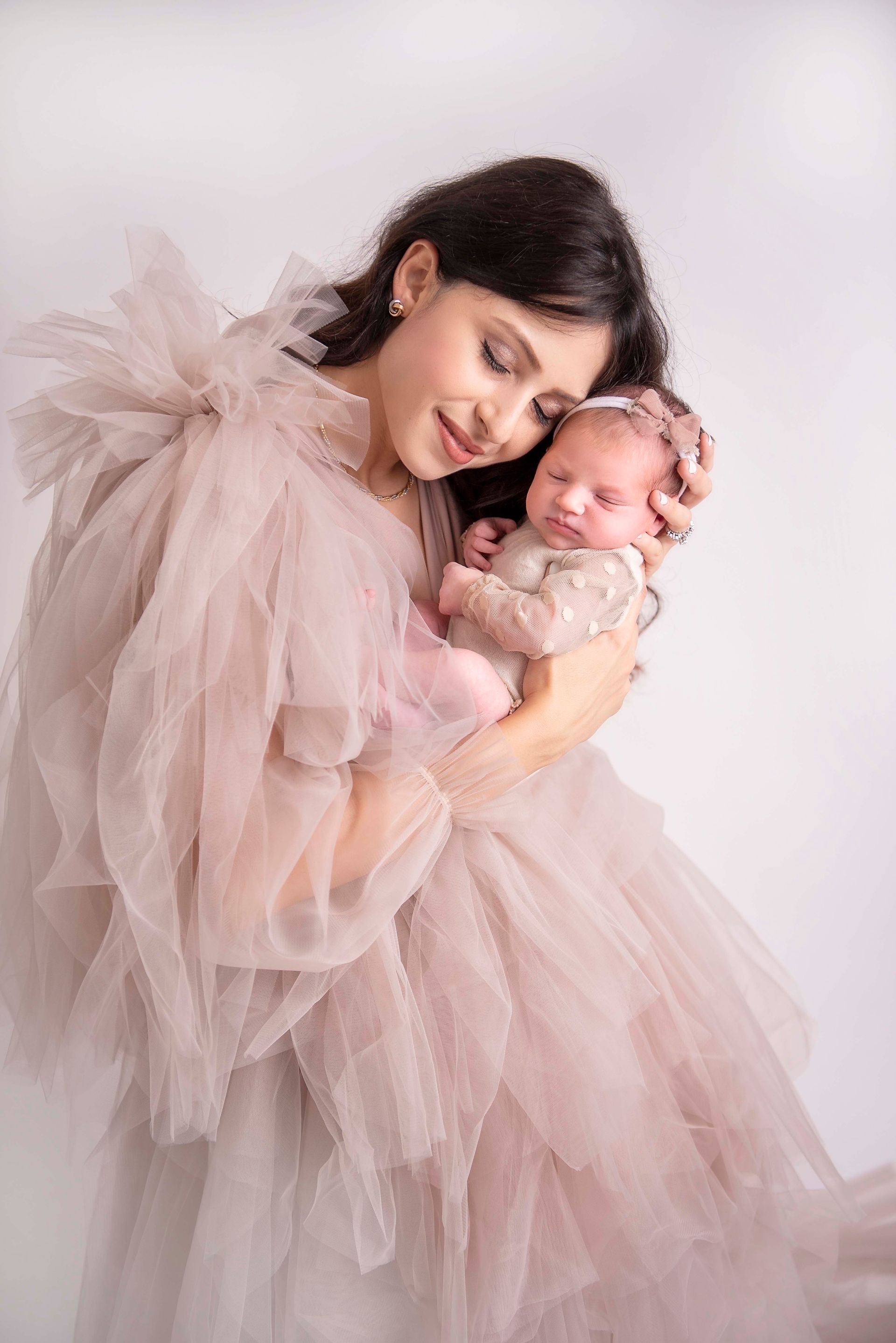 Mother in pink dress cradling newborn baby, both with serene expressions. White background.