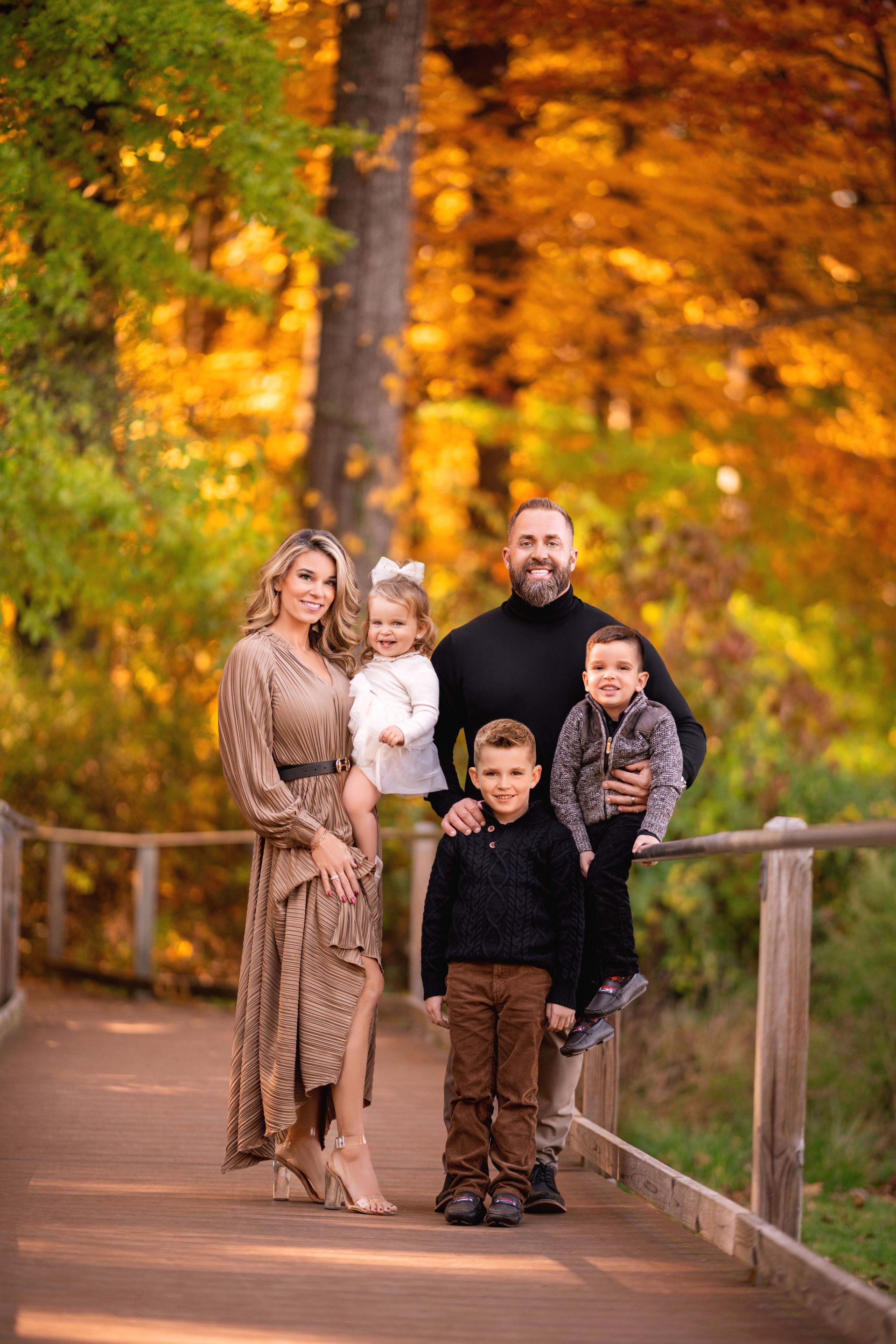 Family of five posing on a wooden bridge surrounded by autumn foliage.