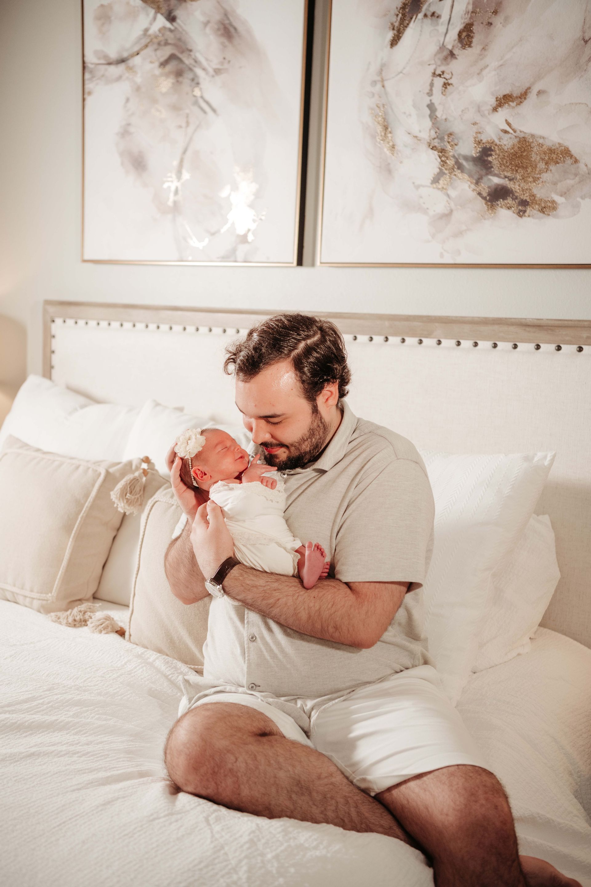 Father holding newborn baby on bed, neutral colors, gentle expression.