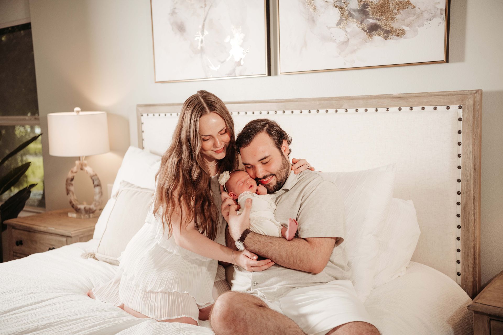 Parents on a bed tenderly hold their newborn baby, surrounded by a cozy bedroom setting.