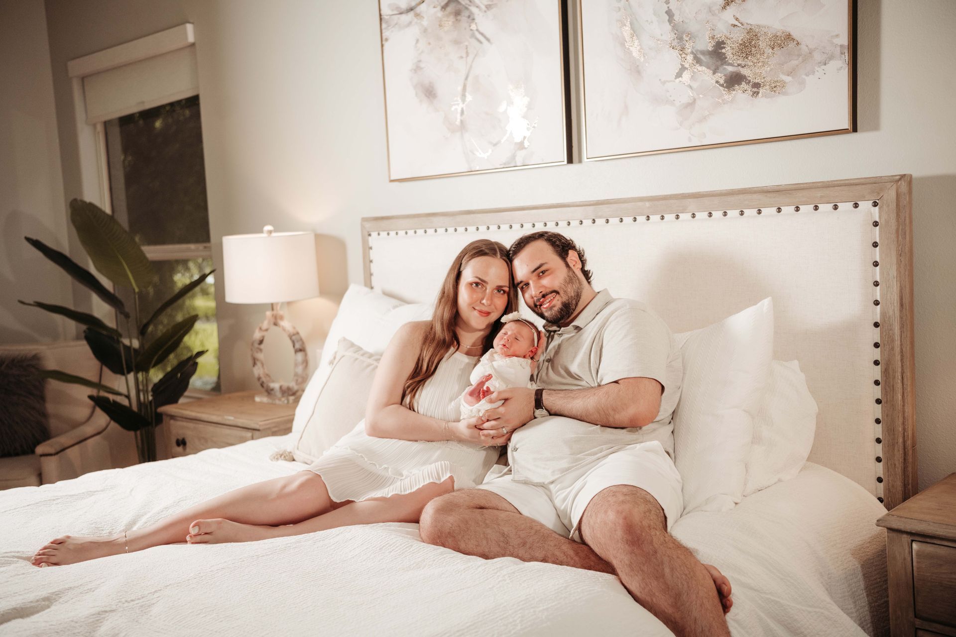 Family of three in a bedroom: parents holding a newborn baby. The parents are sitting on a bed.