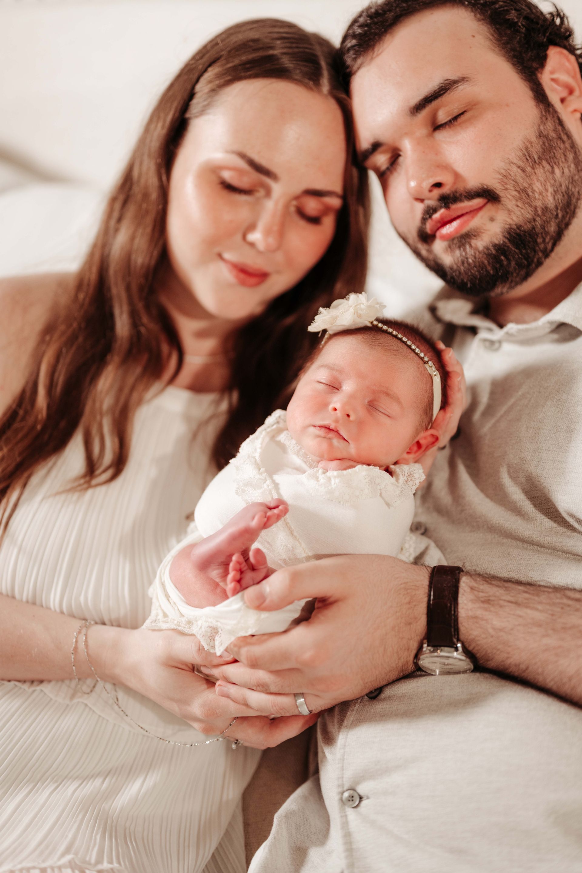 Parents cradling newborn baby, all in white, peaceful expressions.