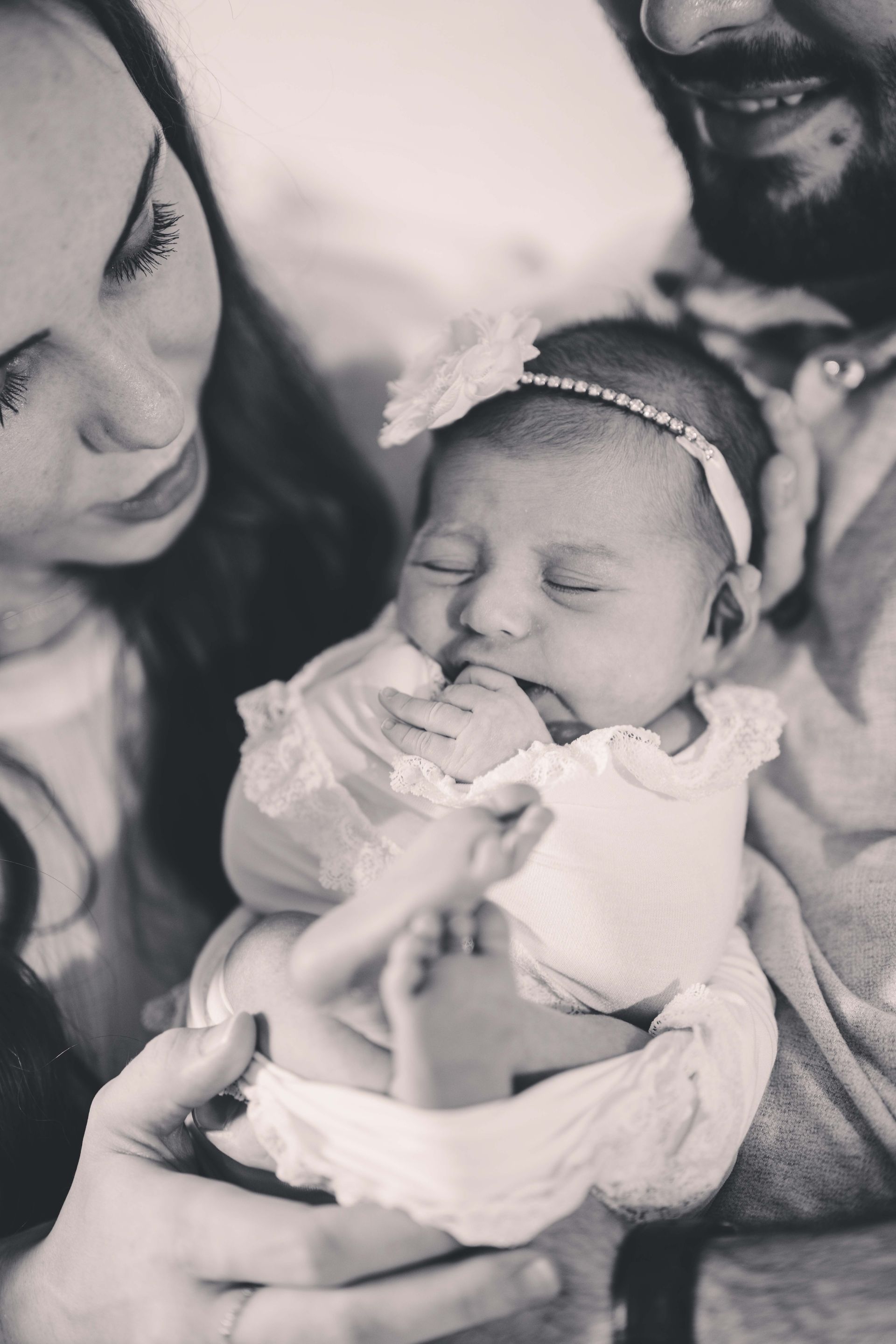 Parents holding newborn baby wearing a headband. Black and white.