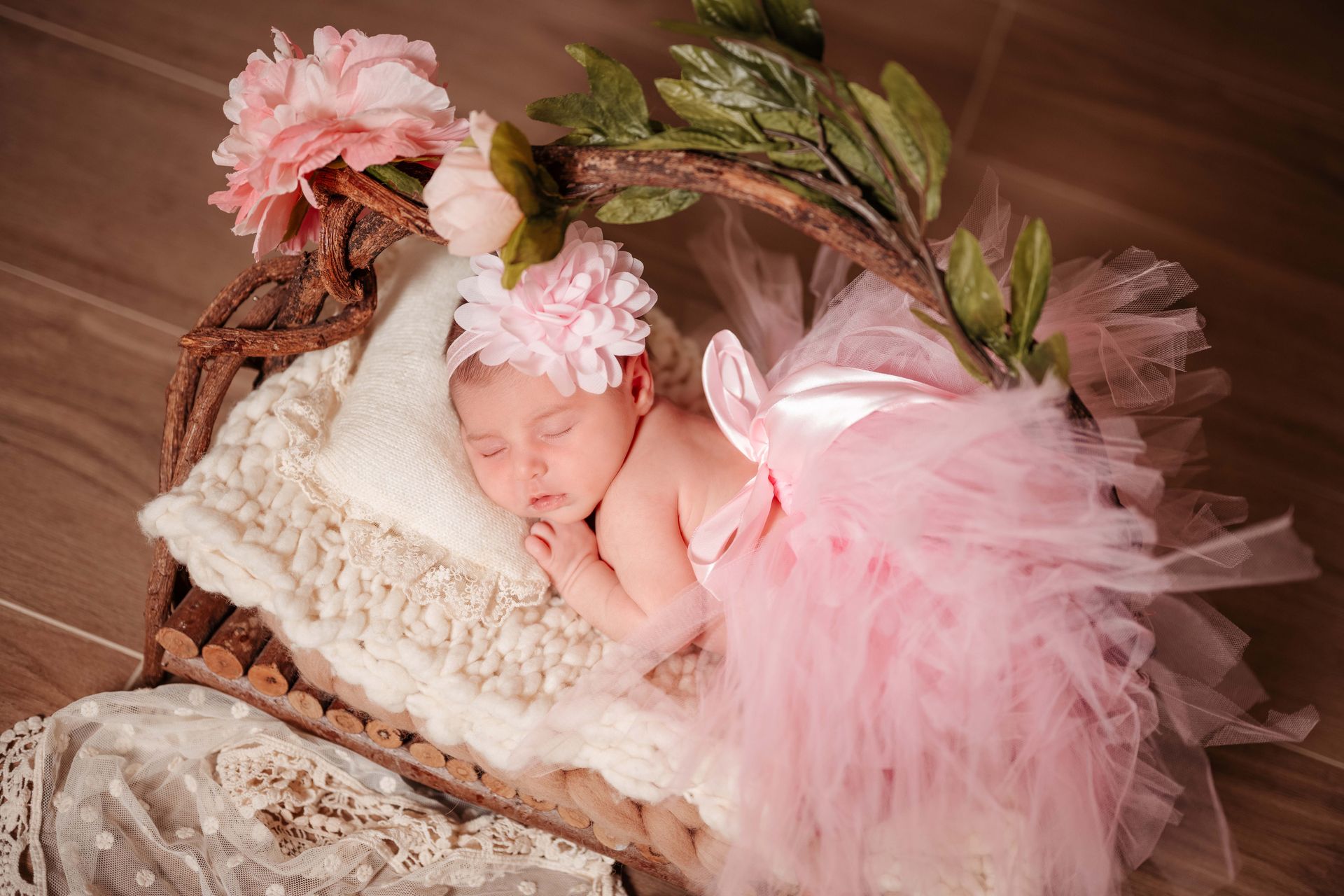 Newborn baby girl sleeping in a decorative bed with pink tutu and floral headband.