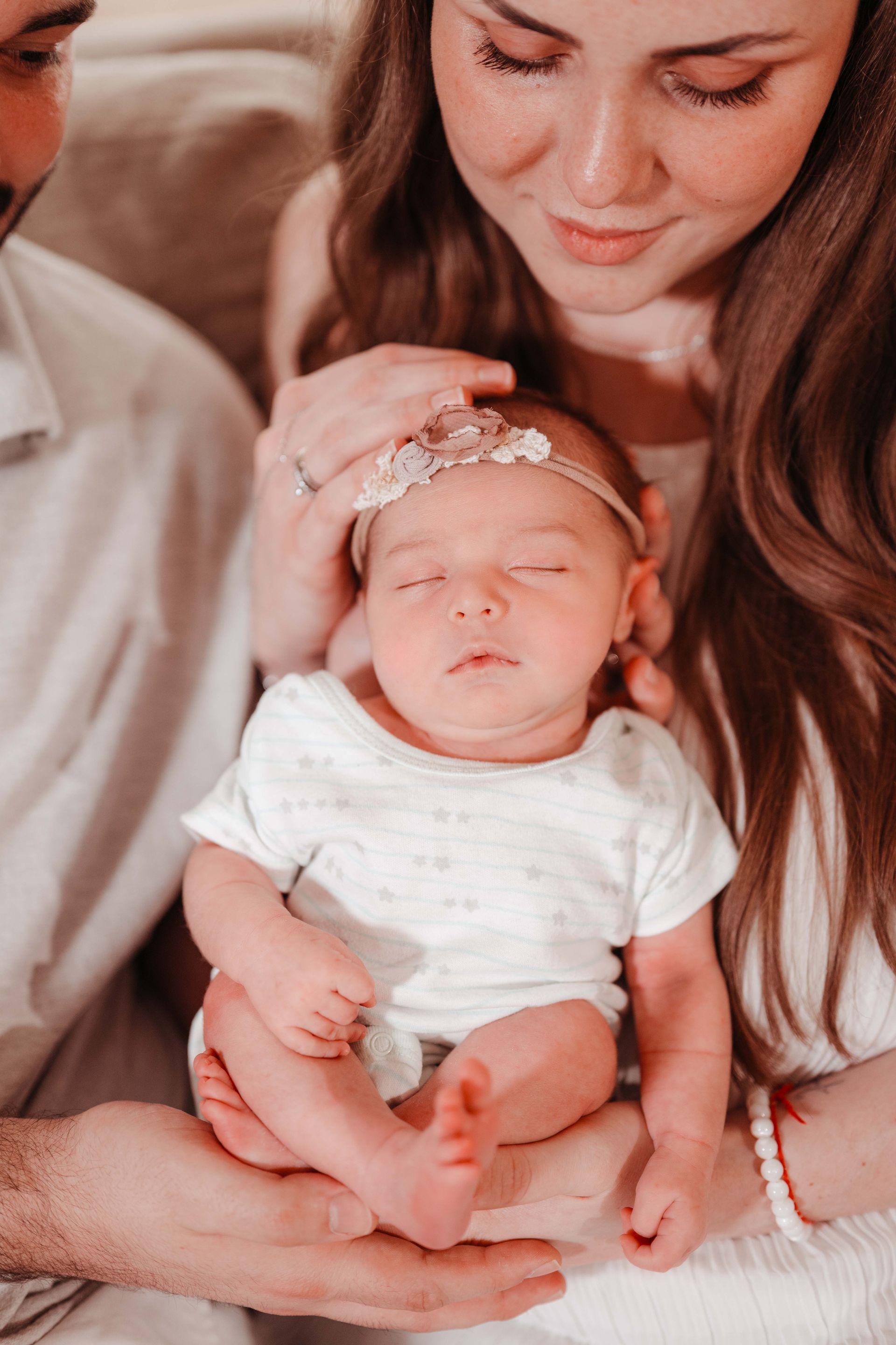 Parents holding a sleeping baby, wearing a headband, close-up shot.