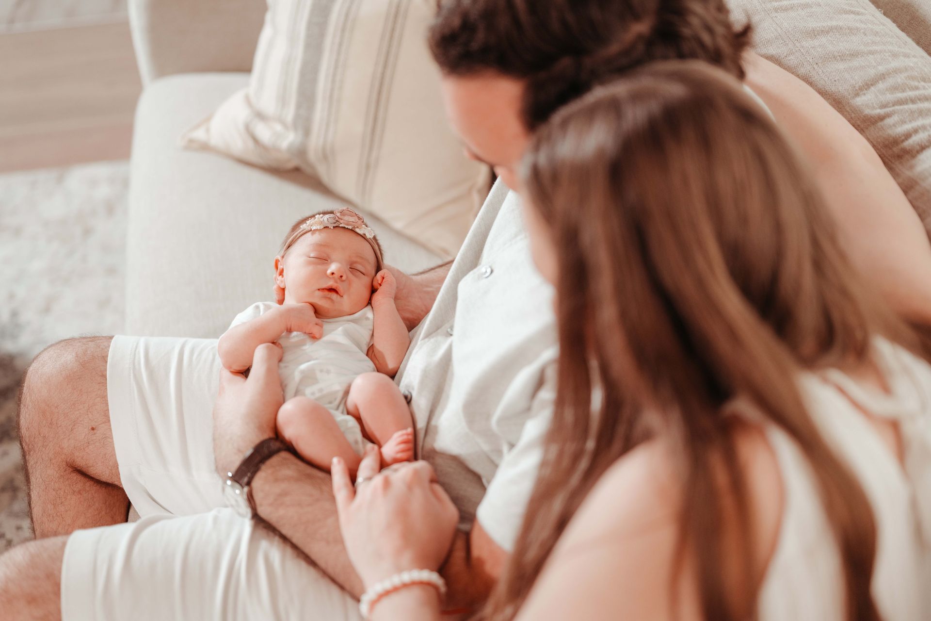 Parents holding a sleeping newborn baby. Soft lighting, neutral colors.