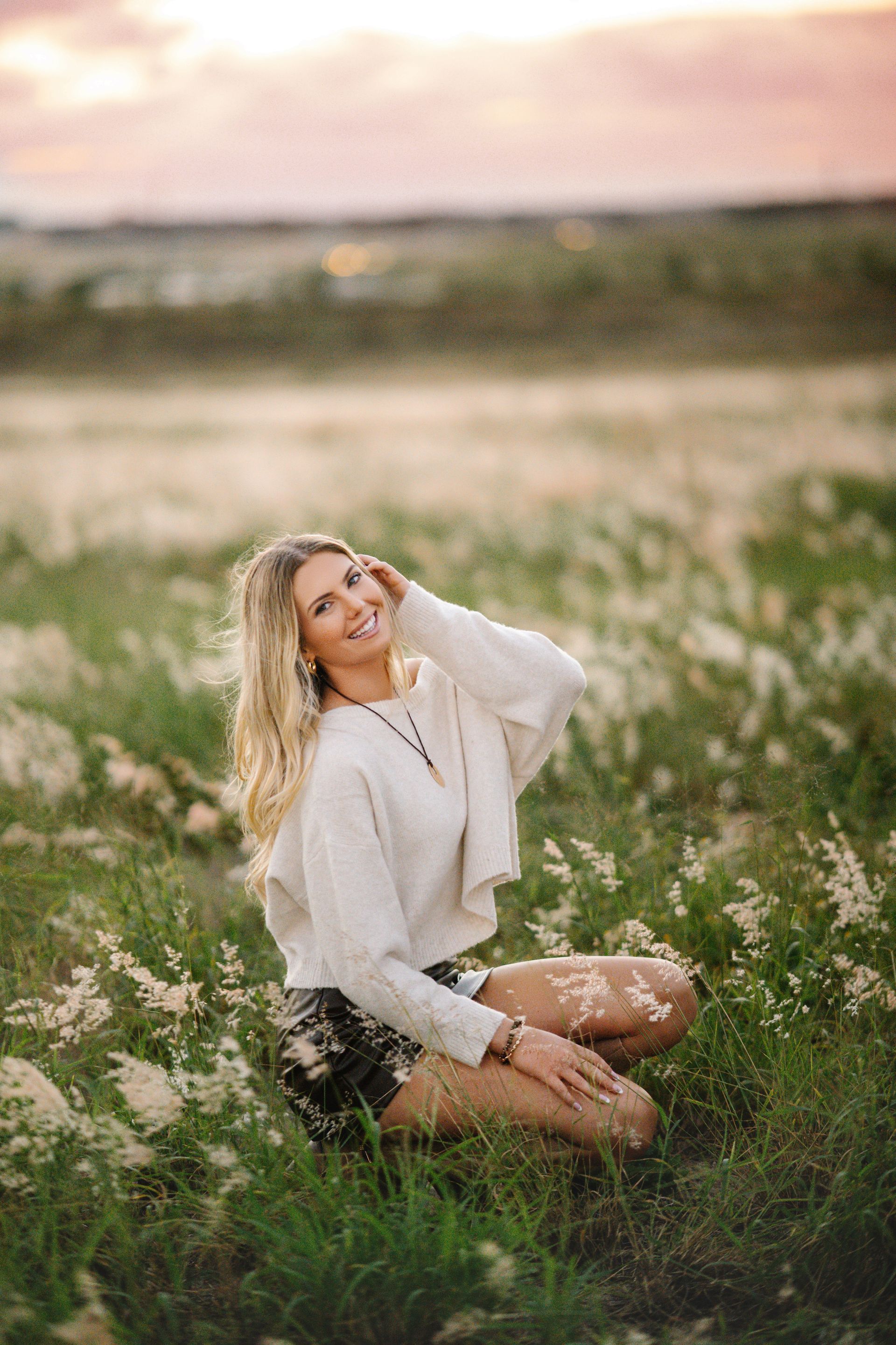 Woman in graduation cap and gown, smiling, outdoors on a wooden walkway.
