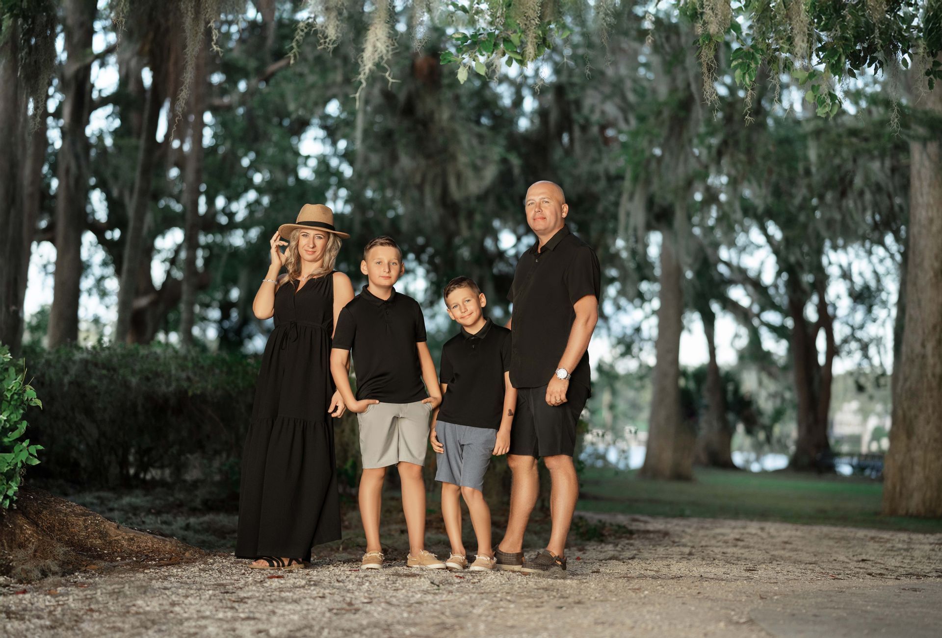 Family of four in black and tan outfits pose in a park with hanging moss.