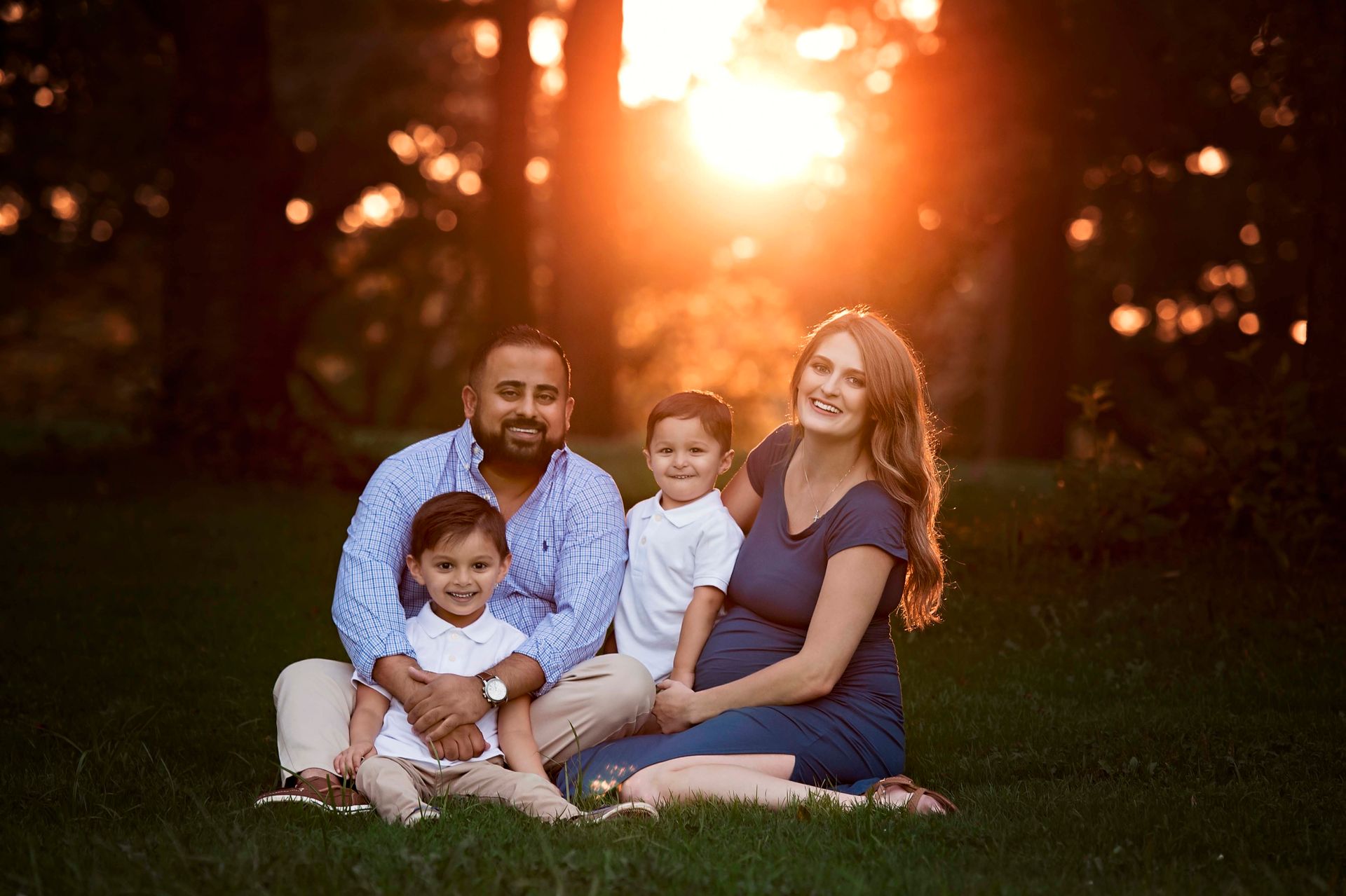 Family of four seated on grass with sunset in background.