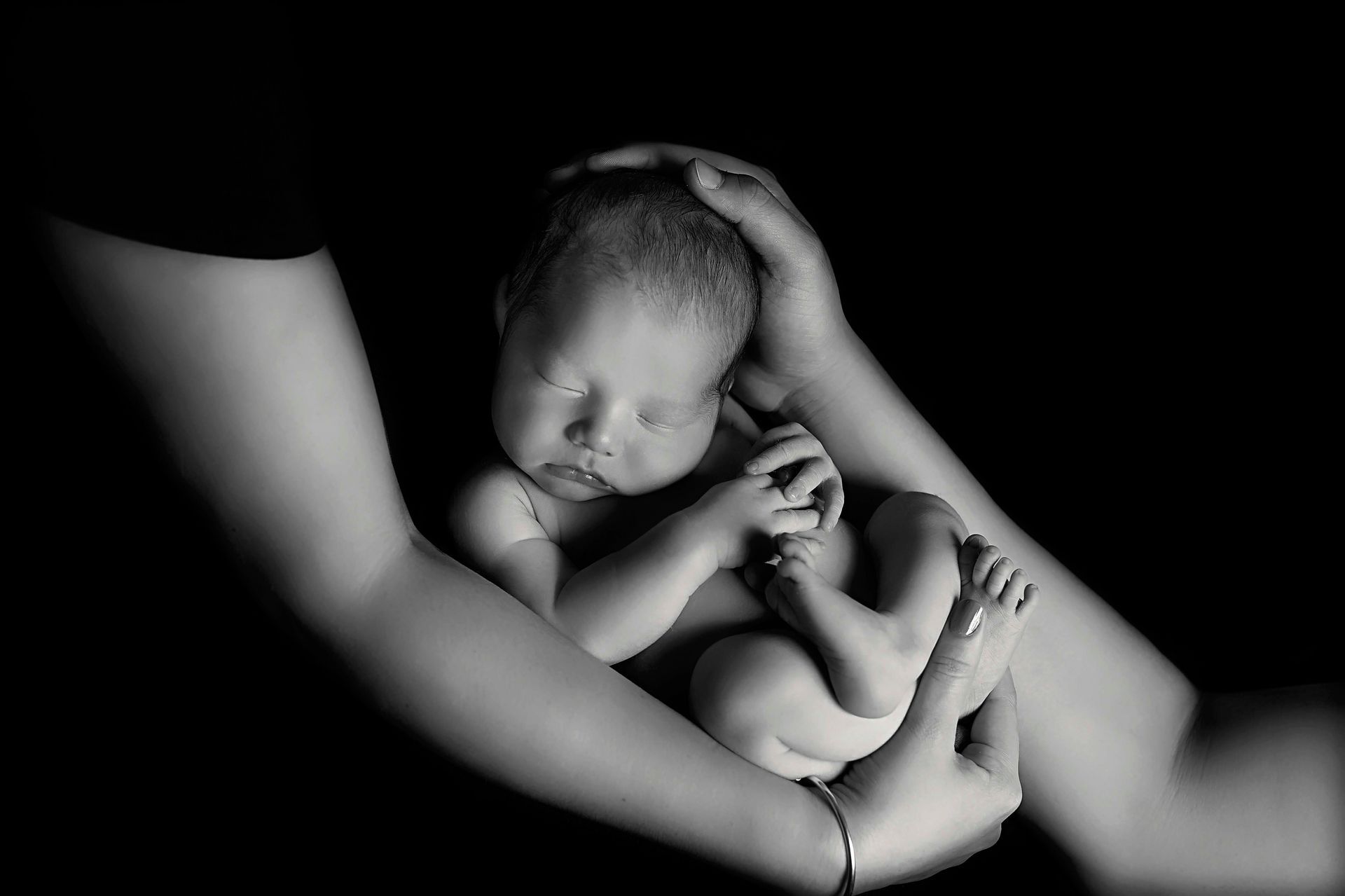Newborn baby held gently in parent's arms, black and white studio shot.