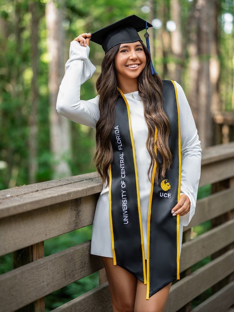 Bride and groom walking hand-in-hand under purple wisteria, brick wall on left, greenery on both sides.