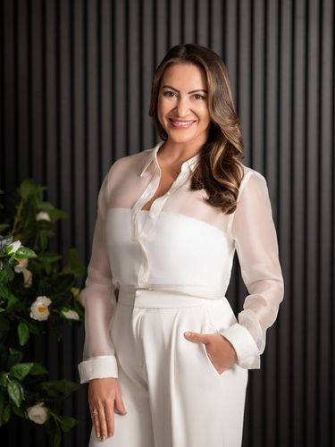 Pregnant woman holding flowers, belly exposed, wearing off-shoulder sweater and open jeans, embraced by someone.