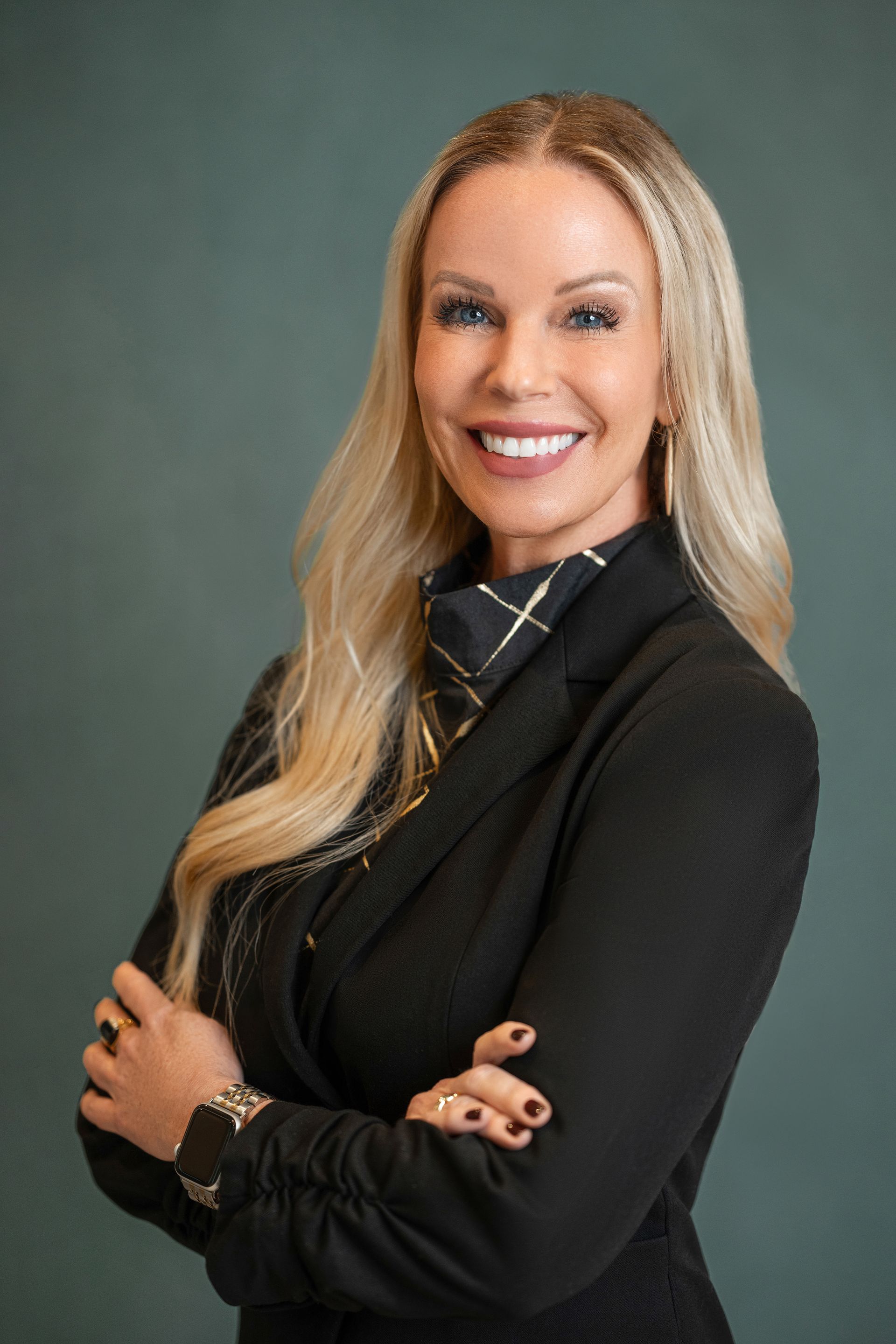 Woman in blue dress smiles, talks on phone, works on laptop at outdoor cafe table.