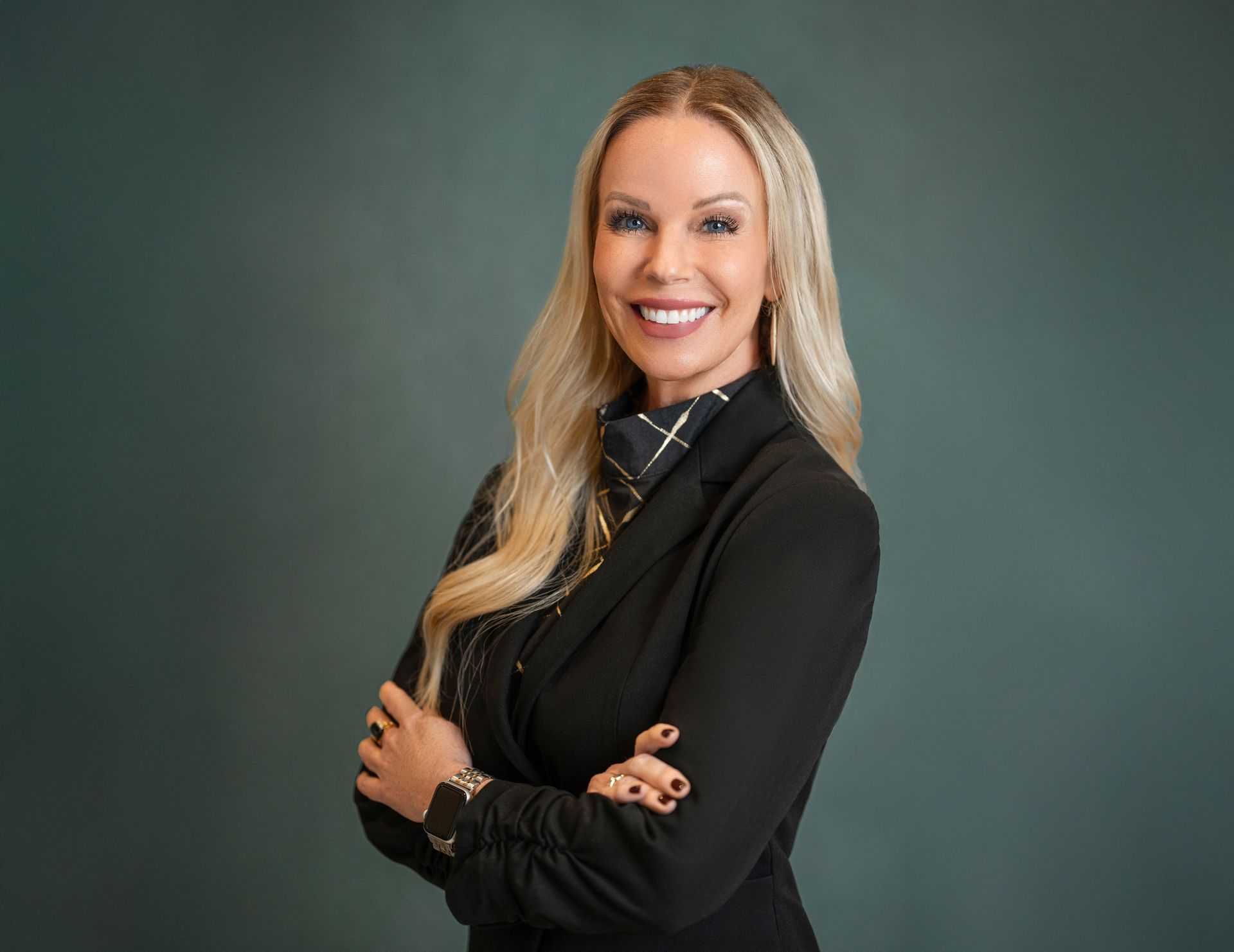 Woman in blue dress smiles, talks on phone, works on laptop at outdoor cafe table.
