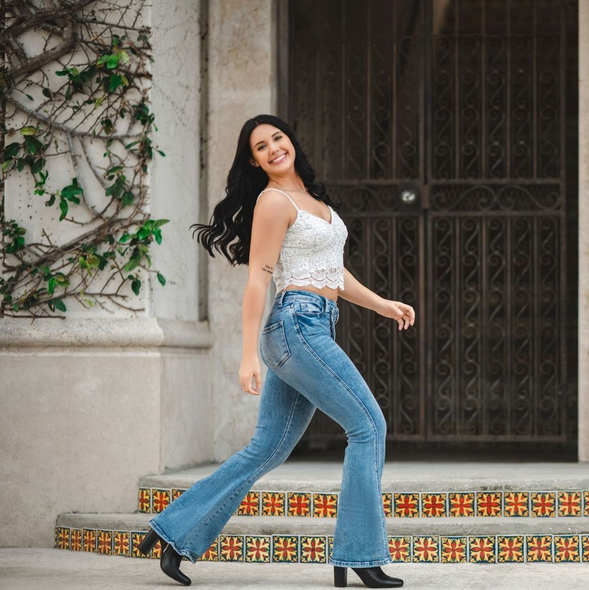 Bride and groom walk hand-in-hand, smiling, under purple wisteria blooms, in a garden setting.