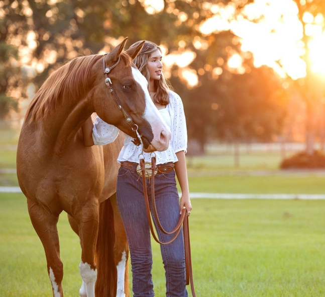 Bride and groom walk hand-in-hand, smiling, under purple wisteria blooms, in a garden setting.