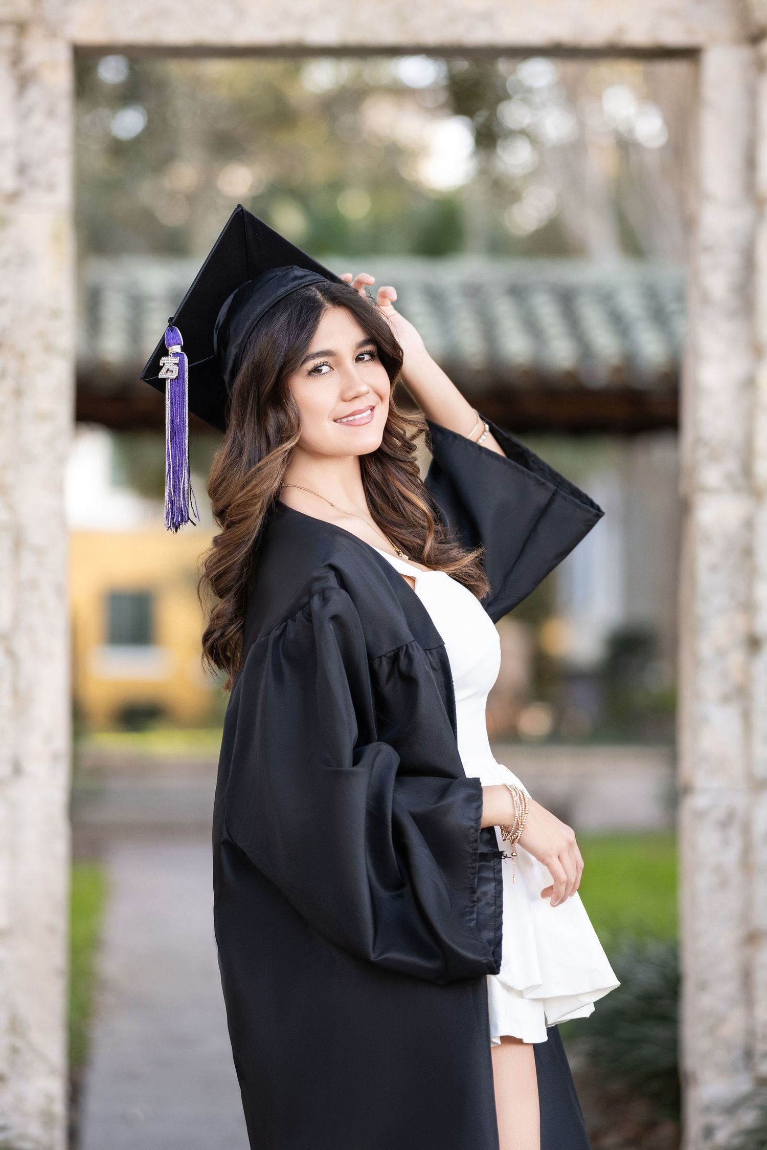 Woman in graduation gown and cap, smiling, standing in an archway, holding cap.