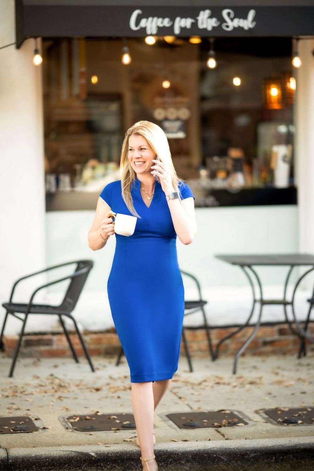 Woman in graduation cap and gown, smiling, outdoors on a wooden walkway.