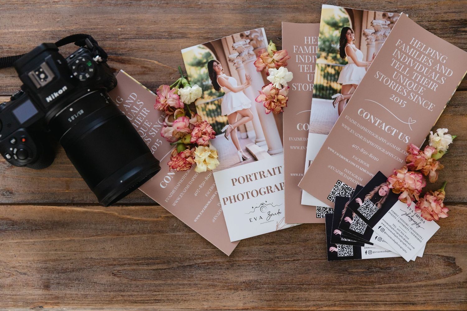 Nikon camera next to brochures with floral arrangements and business cards on a wooden surface.